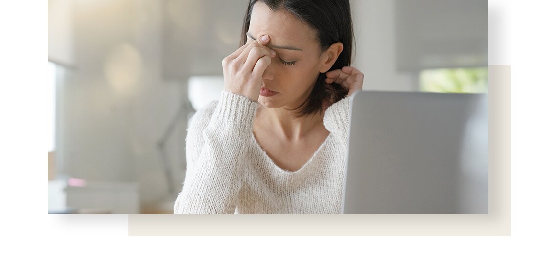 Woman suffering from flatulence in holding her forehead in pain, while sitting next to her computer.