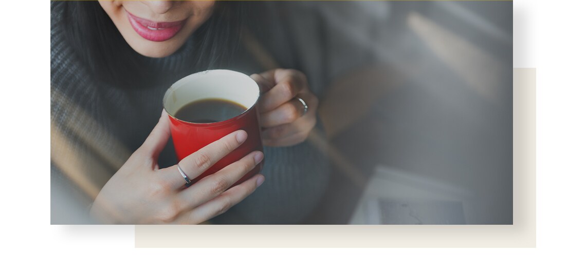 Smiling woman, holding red mug full of coffee.