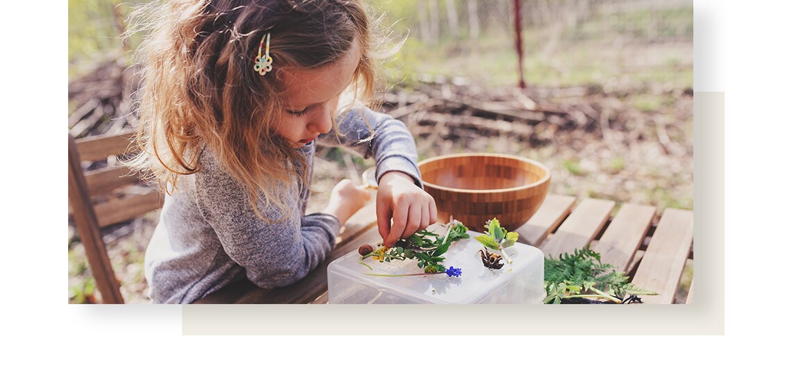 A little girl playing with leaves and flowers on a garden table.