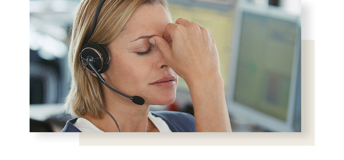 Blond haired woman working in a call centre, holds her forehead in pain, caused by indigestion.
