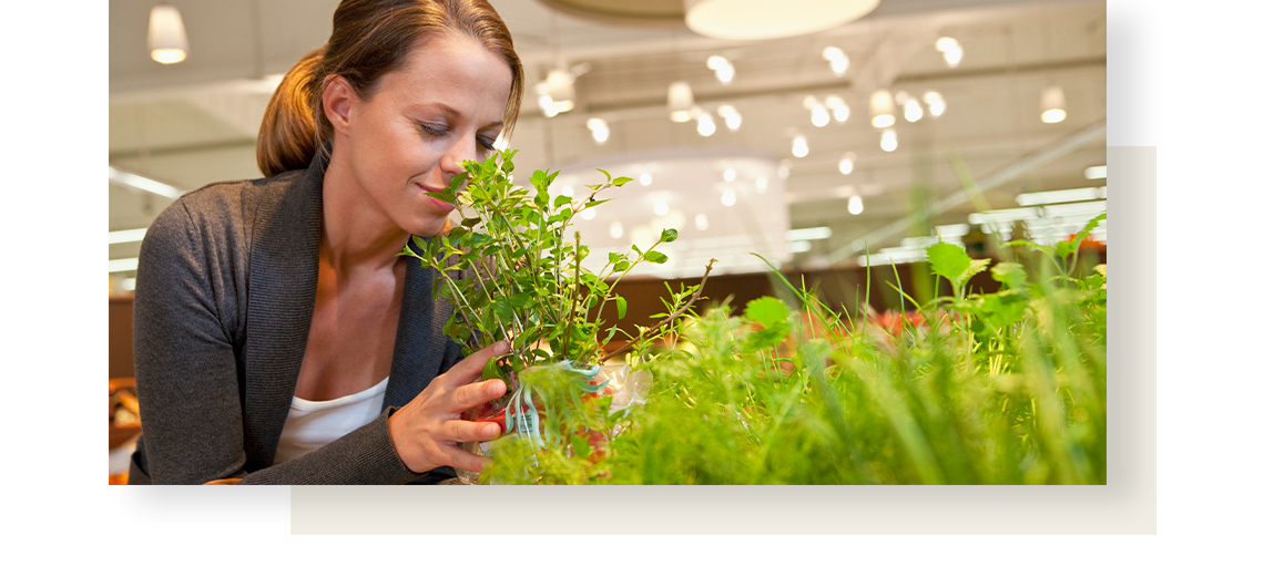 Woman smelling bunch of herbs in groceries store.