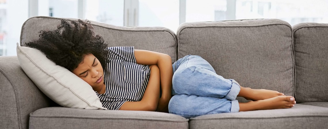 Woman with curly dark hair is lying on the sofa while suffering from irritable stomach.