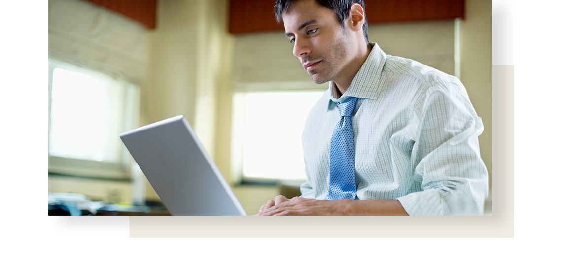 Man, wearing blue tie, working on a laptop.