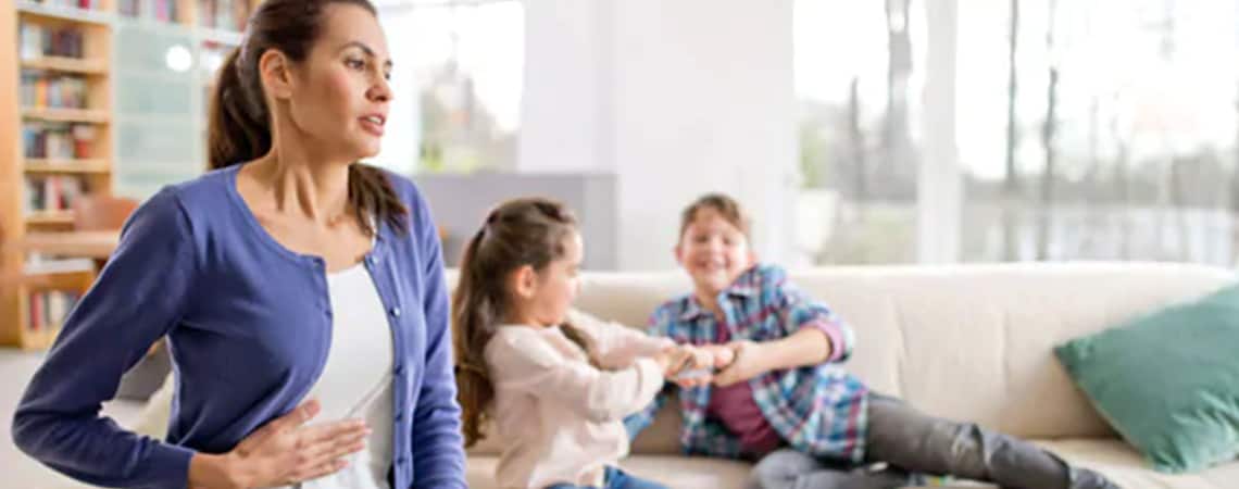 A woman, whose kids are playing in the background, suffering from flatulence.