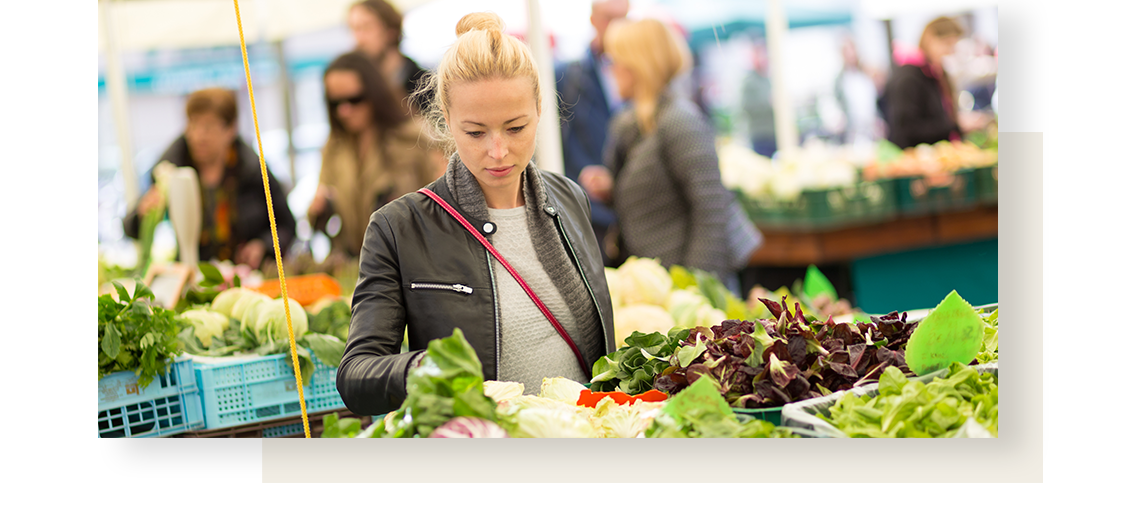 Blond hair woman chooses from various kinds of lettuce, when doing groceries.