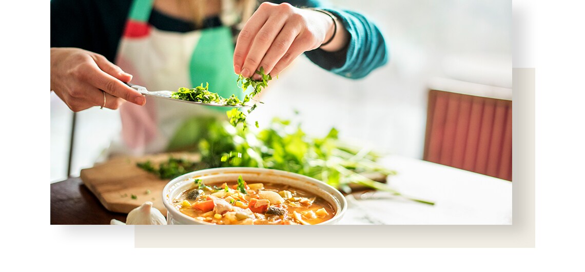 Woman is seasoning the dish, by putting freshly cut green herbs in it.