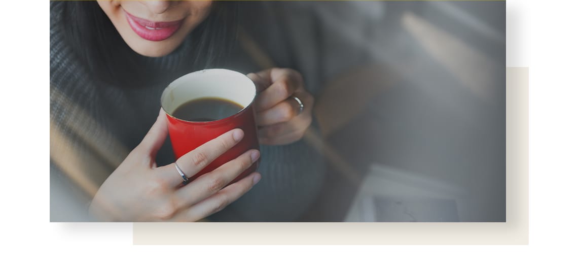 Smiling woman, holding red mug full of coffee.