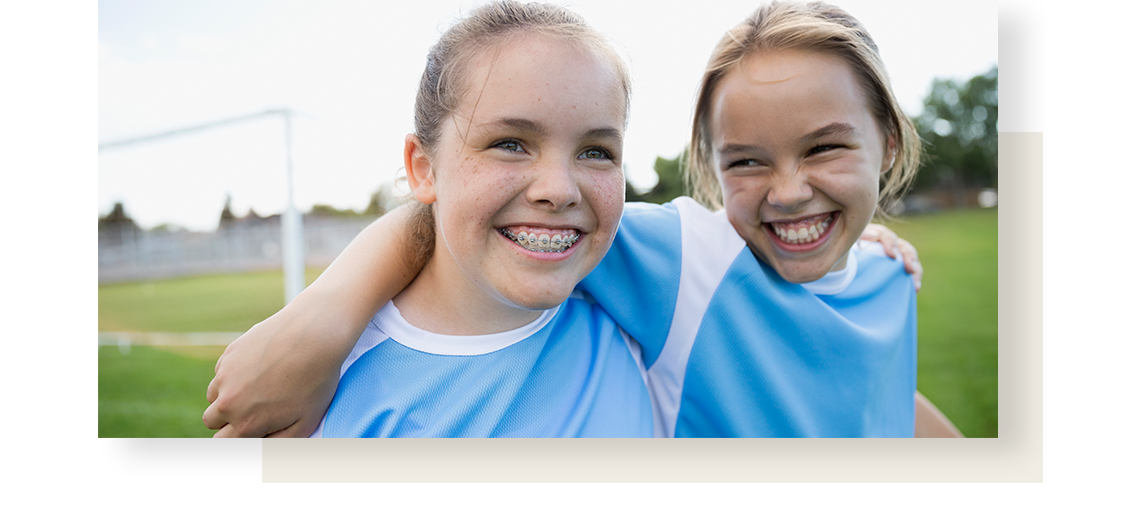 Two joyful teen girls, wearing football gears, holding each other and smiling.