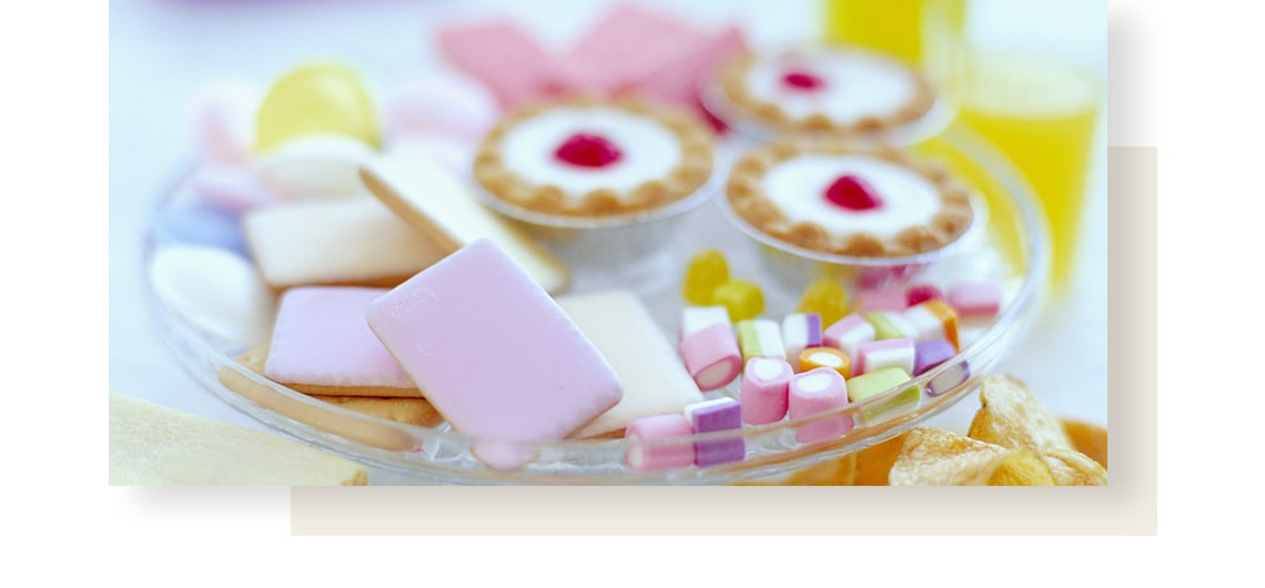Variety of sweets and cookies: donuts, chocolate, marshmallow, macarons, lying on white, stone-like table.