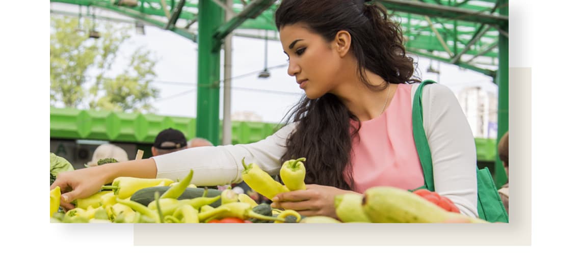 Young woman with long dark hair is choosing from variety of colourful peppers at the street market.