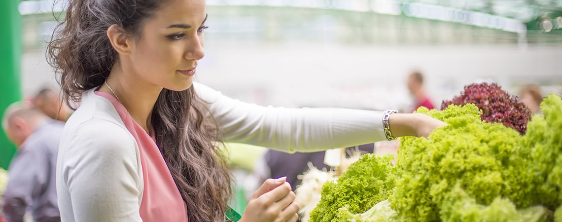 Young woman choosing from various kinds of lettuce while making groceries.