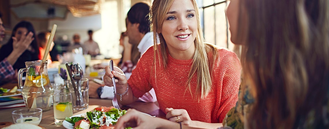 A woman wearing red blouse, is having a meal with her friend, in a casual restaurant
