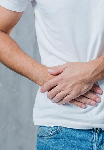 A man dressed in white t-shirt, seen only from hip to shoulder, suffering from stomach pain.