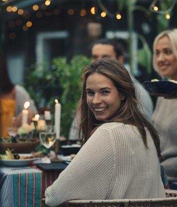 A young woman turns over her shoulder and smiles while sitting at a table with friends.