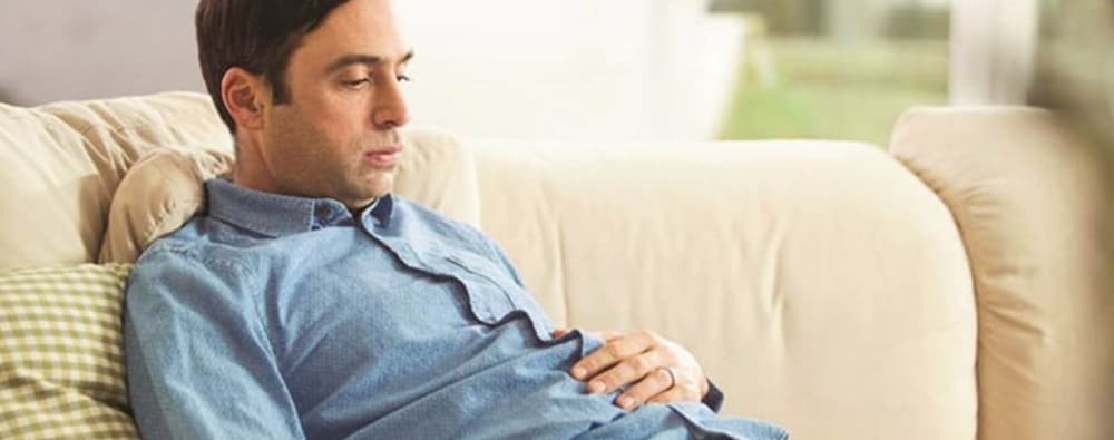 Man wring denim shirt lounging on a sofa, suffering from bloating